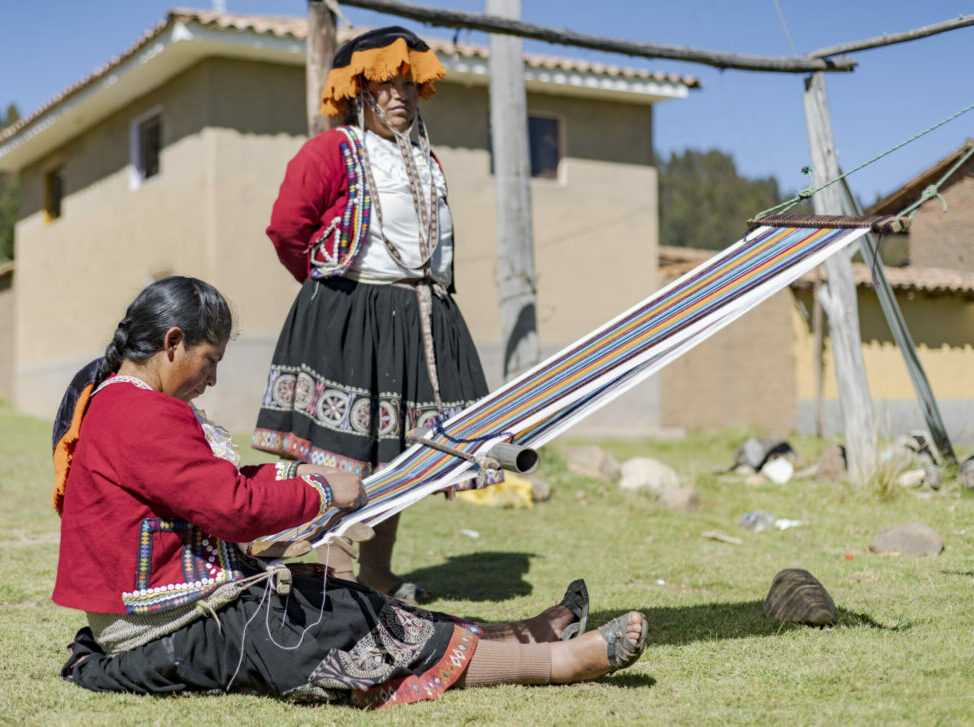 Eine Teilnehmerin von APEDIK in Peru sitzt im Gras und arbeitet an einem Webrahmen