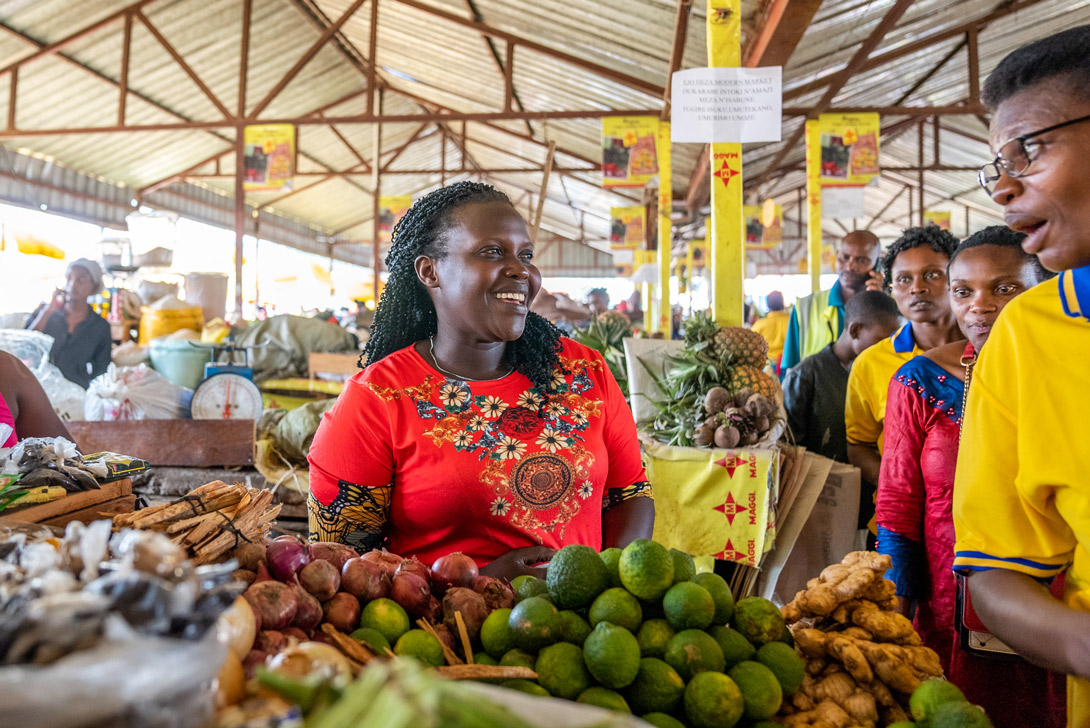 Delphine Nyirahabimana, Teilnehmerin von SYTRIECI in Ruanda lächelt mit ihrem Obst und Gemüse auf dem Stadtmarkt.
