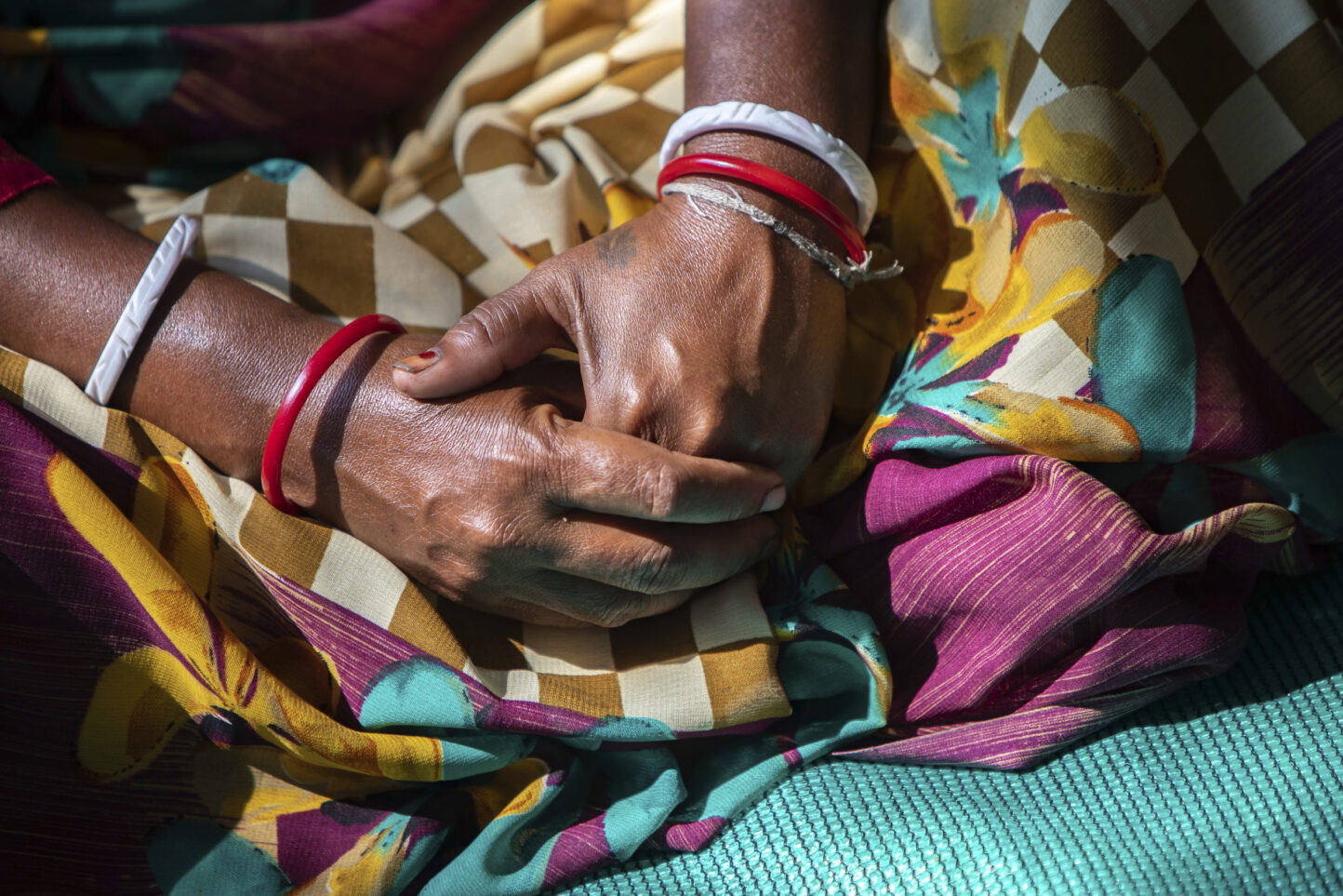 Une Indienne joint les mains sur ses genoux, assise sur un sari. Photo : Adam Dickens